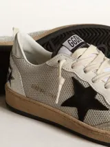 Championes Golden Goose modelo Ball Star, de caña baja, confeccionados en cuero color blanco con detalles en gris y negro. Presentan una estrella negra en el lateral, talón plateado con logo y suela de goma con efecto envejecido.