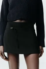 Falda pantalón de tiro medio en color blanco, con diseño minimalista y detalle de cinturón fino integrado con hebilla metálica. Cuenta con cierre lateral mediante cremallera oculta.