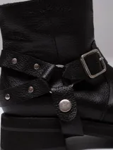 Bota corta de cuero negro con punta cuadrada, suela track y detalle de estribo desmontable con hebilla metálica.