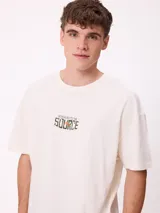 Remera de corte oversize color crema con estampado gráfico en la espalda que muestra un oso, un paisaje natural y el texto 'Stay close to the source'.