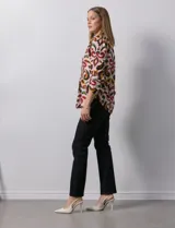 Blusa de gasa estampada con diseño geométrico multicolor, cuello a la base con escote en V y abertura frontal con botones. Presenta detalle de plisado en la parte delantera y mangas largas con sistema de ajuste mediante presilla y botón.
