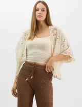 Cardigan abierto estilo kimono, color crudo, con mangas amplias al codo. Presenta una base con textura y motivos florales bordados a tono, con paneles de encaje calado estilo macramé en el frente, puños y ruedo.