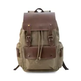 Mochila de tela canvas color negro con solapa y detalles en cuero sintético marrón. Presenta un cierre superior tipo marinero con cordón ajustable, solapa principal con correas y hebillas, y un bolsillo frontal con solapa. Posee bolsillos laterales con cierre metálico y correas de hombro ajustables.