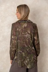 Blusa de gasa con estampado abstracto en tonos verdes y marrones, con detalles de hilos dorados. Presenta cuello camisero con escote en V, mangas largas con puños elásticos y un corte holgado.