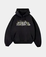 Canguro oversize de color negro con capucha y bolsillo frontal tipo canguro. Presenta un estampado gráfico central con estilo graffiti que incluye elementos urbanos y detalles en amarillo.