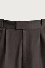 Bermuda de corte relaxed fit color marrón, con pliegues frontales, bolsillos laterales y detalle de bolsillos traseros de vivo, además de bolsillo cerillero. Cuenta con cierre frontal con cremallera y gancho metálico oculto.