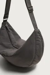 Bolso de hombro tipo hobo de nylon negro, con diseño curvo y asa ajustable. Cuenta con compartimento principal con cierre de cremallera y bolsillo interior con cremallera.