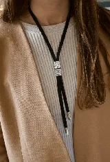 Corbatín estilo bolo tie con cinta de tela negra y dos piezas metálicas cuadradas con diseño de espiral en relieve, finalizado con punteras metálicas plateadas.