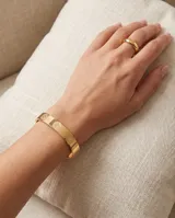 Esclava rígida de acero con baño de oro, diseño de superficie lisa con grabados circulares del símbolo de San Benito.