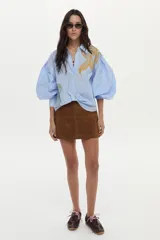 Camisa de algodón a rayas celestes y blancas, con mangas abullonadas y gran estampado floral en el frente.