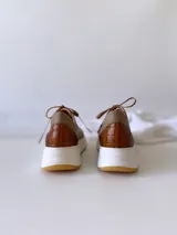 Championes de cuero color visón con cordones marrones, suela blanca y base color caramelo.