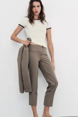 Pantalón capri de tiro medio con raya diplomática en tonos beige y marrón. Presenta trabillas, bolsillos laterales y cierre frontal con cremallera y botón metálico.