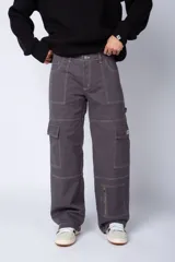 Pantalón tipo carpintero de corte relaxed fit y tiro medio, confeccionado en denim negro con costuras a contracolor en blanco. Presenta múltiples bolsillos cargo laterales, un bolsillo con cierre en la parte inferior y presillas utilitarias.