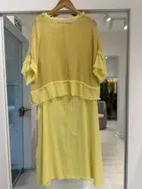 Vestido midi amarillo de corte recto, con superposición de tela de red en la parte superior y detalles de flecos en los bordes.