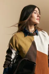 Sweater de tejido de punto con diseño geométrico de bloques de color en tonos tierra, marrón, ocre y blanco. Presenta cuello redondo, mangas largas y un corte relajado.