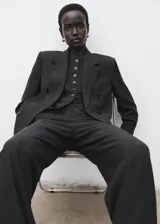 Pantalón de traje de tiro medio, color negro, de diseño recto y largo, con cierre frontal de cremallera, botón y ganchos ocultos con tapeta, y bolsillos laterales.