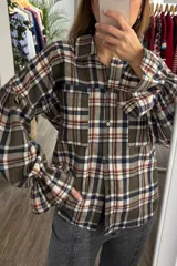 Camisa de manga larga con estampado de cuadros en tonos verde, beige y azul. Presenta cuello clásico, cierre frontal con botones, dos bolsillos delanteros y mangas con puños elásticos y detalle de volado.
