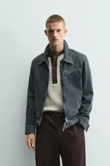 Cazadora cropped fit de denim de algodón, color negro lavado. Presenta cuello solapa, manga larga con puños abotonados, cierre frontal de cremallera y bolsillo superior con cierre de cremallera en el pecho.