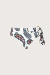 Calzón de bikini tipo faja de tiro alto, color blanco con estampado paisley en tonos azul, rojo y mostaza. Cuenta con una argolla metálica decorativa y un lazo lateral.