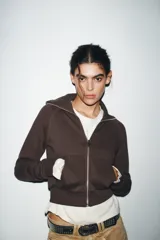 Chaqueta de felpa negra con cuello solapa, manga larga con puño, bolsillos de plastrón en el delantero y cierre frontal con cremallera.