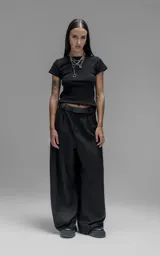 Pantalón sastrero de corte oversize, color negro, con pinzas frontales que forman tablones profundos, cintura ancha, presillas robustas y bolsillos laterales y traseros tipo ojal.