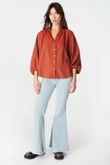 Camisa de corte holgado y diseño minimalista, color crudo, con cuello mao, cierre frontal de botones y mangas largas abullonadas con puños elásticos.