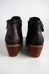 Bota corta de cuero negro con diseño combinado, punta fina y taco geométrico de madera. Presenta detalles en textura croco, apliques laterales con cierre, detalles metalizados y talón con acabado texturizado.