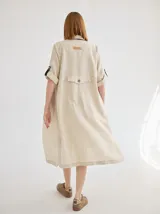 Vestido camisero midi de lino color beige, con diseño de manga corta con solapa, cuello camisero, bolsillo trasero con solapa y botón, y aberturas laterales en el ruedo.