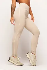 Calza deportiva de cintura alta color beige con detalles de vivos blancos a lo largo de las piernas.