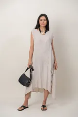 Vestido midi de lino color beige, sin mangas y con cuello redondo. Cuenta con un diseño irregular con detalle de volado vertical a un costado.