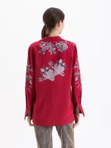 Camisa de manga larga color rojo, con cuello clásico y cierre frontal de botones. Presenta un estampado artístico que combina motivos florales en tonos rosados con ilustraciones de alfileres de gancho.