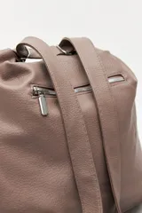 Cartera convertible en mochila, confeccionada en cuero sintético texturizado color marrón. Presenta un diseño con recortes, bolsillo frontal con cierre diagonal, herrajes metálicos plateados, asa superior y correas regulables.