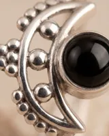 Anillo de plata 925 con diseño de media luna y piedra central de ónix negro. Presenta detalles de pequeñas esferas metálicas en el contorno.