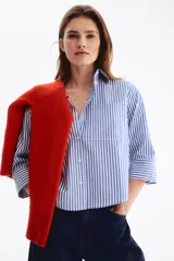 Camisa corta oversize de popelina de algodón con rayas verticales blancas y azules, cuello clásico, cierre frontal de botones, bolsillo en el pecho y mangas tres cuartos con puños anchos.