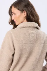 Campera de sherpa color beige con cierre frontal de botones a presión y cuello camisero. Presenta un diseño de textura afelpada con detalles de ribetes en la solapa y puños.