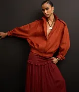 Falda midi evasé color borgoña de poliéster satinado, con cierre trasero invisible, volado en la cadera y ruedo fruncido.