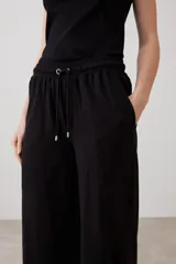 Pantalón de corte amplio y tiro medio, confeccionado en tejido suave de color negro. Presenta una cintura elástica con cordón ajustable y bolsillos laterales amplios.