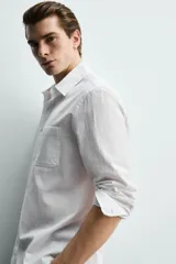 Camisa de corte regular fit color blanco, confeccionada en tejido de algodón con efecto arrugado, con cuello solapa, manga larga, puños abotonados y un bolsillo de parche en el pecho.