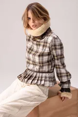 Blusa de tartán con diseño versátil, confeccionada en tela escocesa con detalles en cuero de oveja. Presenta cuello alto con forro de piel sintética, mangas largas con puños de cuero y piel, y un ruedo tableado con ajuste de cinturón de cuero en la cintura.