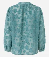 Camisa celeste en tejido chiffon con textura de bordado con felpas, cuello mao, abotonadura frontal y mangas largas abullonadas.