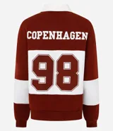 Saco de tejido de punto color bordó y blanco, con cuello polo blanco y tapeta de botones. Presenta un estampado de texto en el pecho.