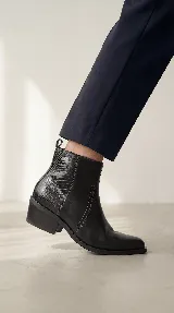 Bota corta tipo chelsea de cuero negro, con panel lateral texturizado y taco cuadrado bajo.