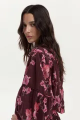 Blusa bordó con estampado floral en tonos rosados, confeccionada en algodón Swiss Dot, con mangas largas abullonadas y escote en V con botones frontales.