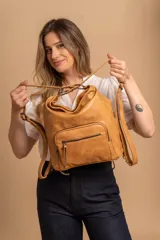 Cartera mochila color tostado, de cuero sintético, con compartimento principal amplio y bolsillos frontales con cierre. Tiene correas ajustables y asa superior para llevar al hombro o como mochila.