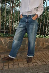 Pantalón de jeans estilo relaxed fit, de tiro alto, color azul con efecto lavado y botamanga con vuelta. Cuenta con cinco bolsillos, trabillas para cinto y cierre frontal con cremallera y botón metálico.