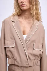 Cazadora color beige con bordados en hilo blanco en cuello, bolsillos y puños.
