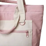 Bolso tipo tote bag color rosa con bolsillo frontal y asas en tono crudo. Cuenta con tiras largas para el hombro y asas cortas de mano, además de un bolsillo delantero con cierre y detalle de argolla metálica.