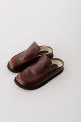 Zueco de cuero color marrón oscuro, con costuras decorativas en hilo rojo en el empeine y suela plana de goma.