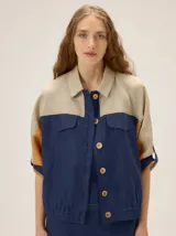 Chaqueta de lino de corte holgado con diseño color block en tonos beige, azul marino y mostaza. Cuenta con cuello camisero, bolsillos con solapa en el pecho, mangas cortas y cierre frontal con botones.
