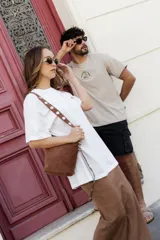 Cartera tipo bandolera de color negro, confeccionada en cuero sintético con acabado aterciopelado. Cuenta con una correa larga ajustable decorada con remaches metálicos circulares.